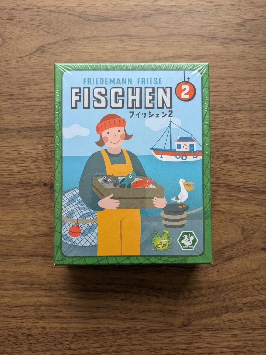 机に置いた『フィッシェン2』の箱の表。緑の網目の地に、魚の入った木箱を抱えた漁師の絵